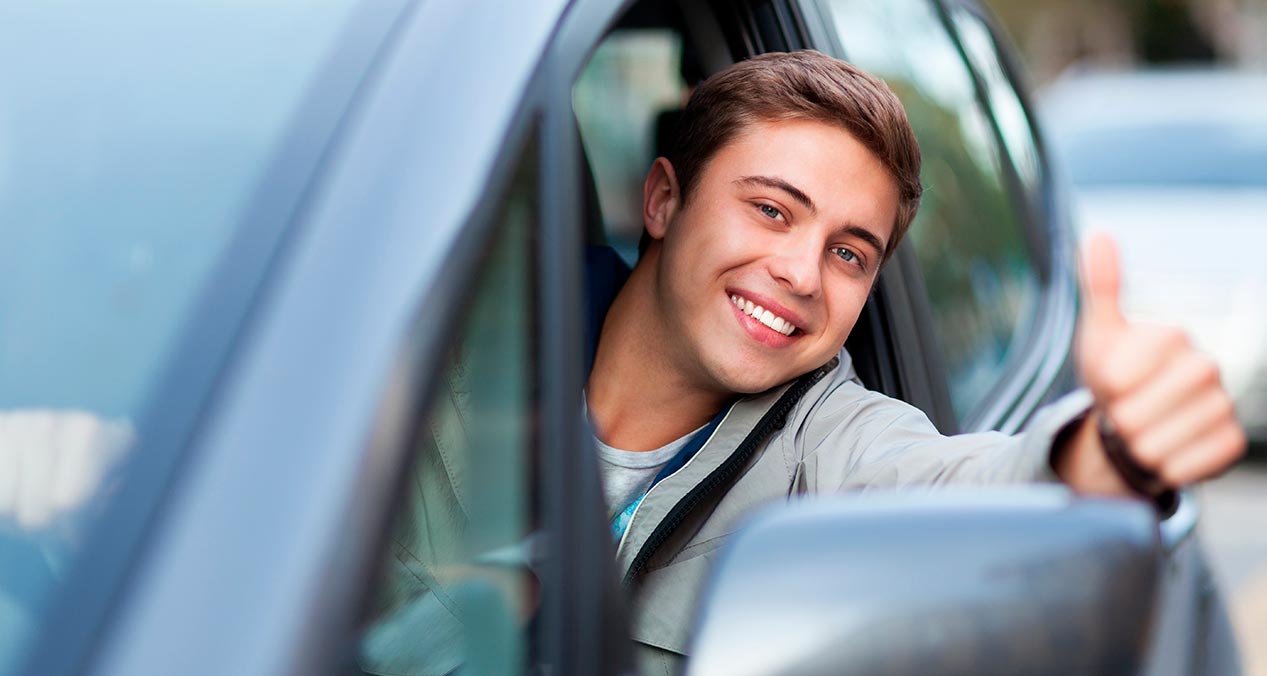 Hombre sonriente se asoma desde la ventanilla de un auto y levanta su pulgar 